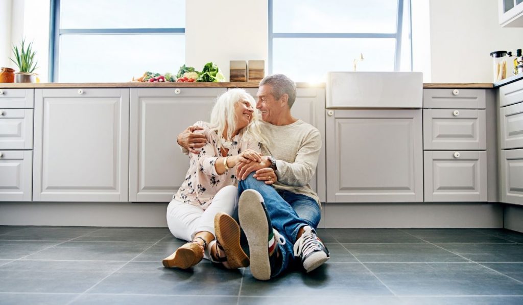 cute senior couple smiling at each other while sitting on the kitchen floor